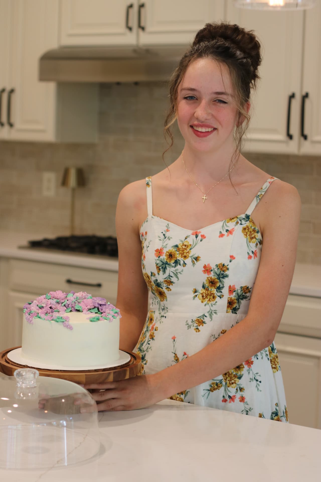Hannah in a floral dress holding a white cake decorated with purple piped flowers
